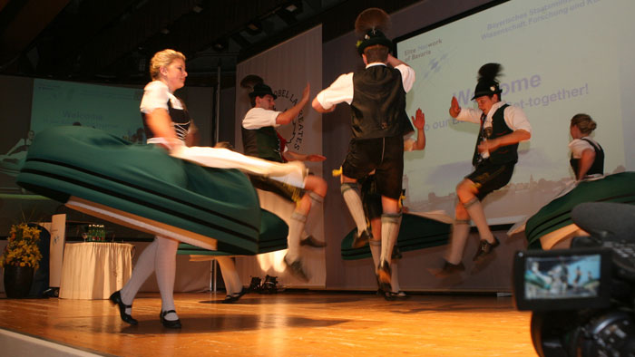 Gruppenbild: In bayerische Tracht gekleidete Personen schuhplatteln und tanzen.