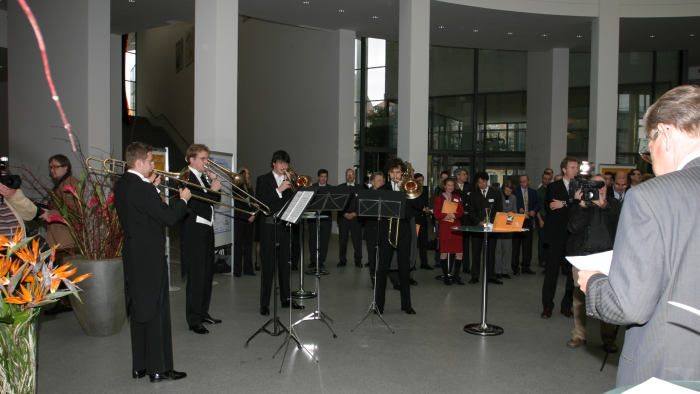 Gruppenbild: Ein Blechbläser-Ensemble spielt vor Zuschauerinnen und Zuschauern ein Musikstück.