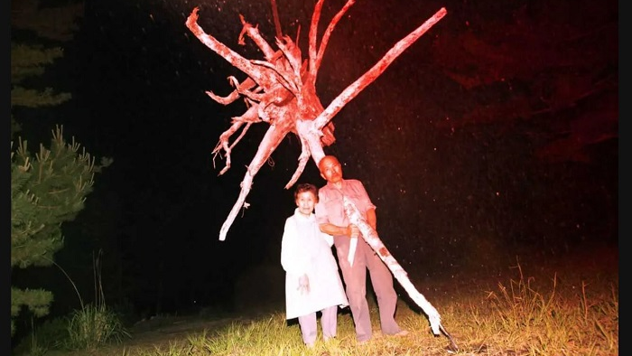 Ein älteres Paar auf einer Wiese. Ein Baum wächst durch die Brust eines Mannes.