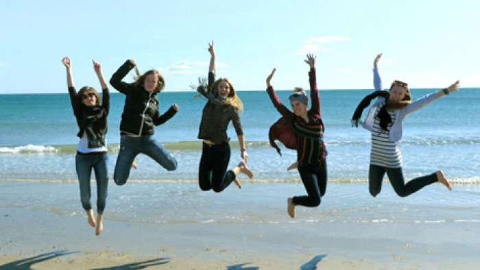 Photo of numerous students at a beach, leaping into the air.