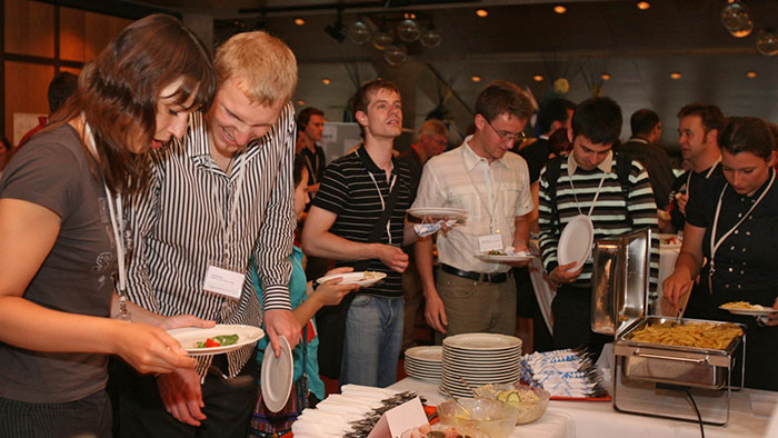 Some attendees stand and chat in front of a buffet.
