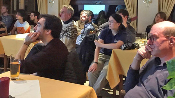 A group of people sitting around a rectangular table and listening to a speaker outside the image. 