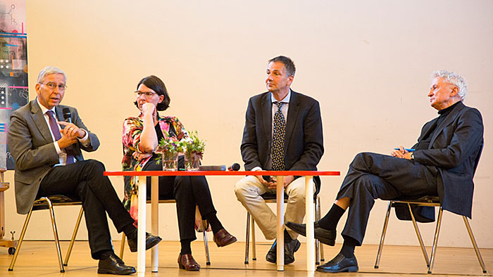 Panel discussion: a woman and three men sit on a stage and discuss an issue. 