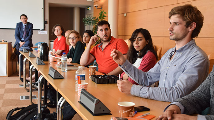 Junge Menschen tauschen sich in einer Unterrichtssituation intensiv in einem Sitzungssaal aus.