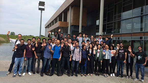 A group of young people standing in front of a building and waving into the camera 