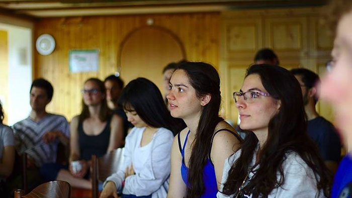 Group picture of students in a wood-paneled seminar room, listening to a presentation. The speaker is not visible.