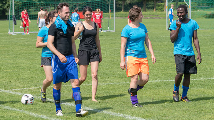 Group photo: several people engaged in a relaxed conversation, walking along the touchline of a football pitch.