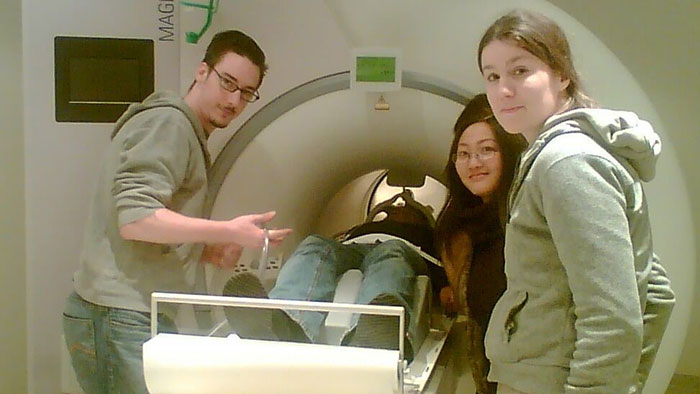 Three persons preparing a brain imaging investigation by means of an MRI scanner.