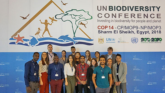 Gruppenbild: Eine Gruppe junger Menschen steht vor einem Banner mit der Aufschrift „UN Biodiversity Conference“. 