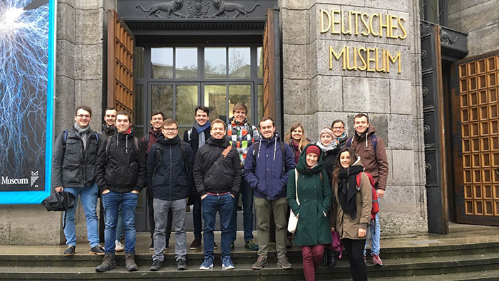 Gruppenbild: Junge Menschen stehen vor dem Eingang zum Deutschen Museum in München und lachen in die Kamera.