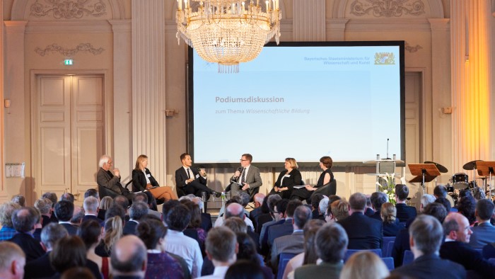 Listeners follow a discussion between six people in a representative hall.