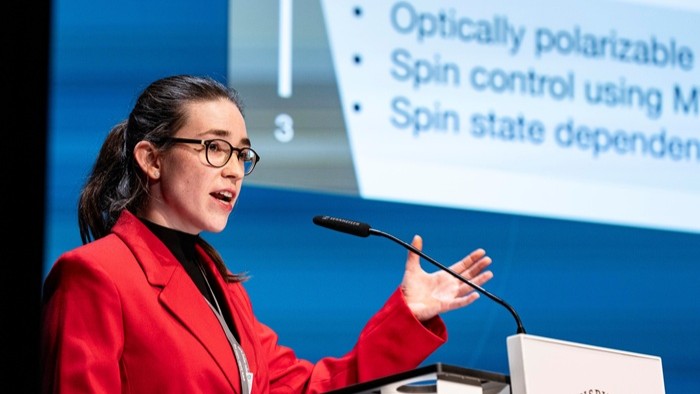 A young woman speaks at a lectern in front of a projection screen.