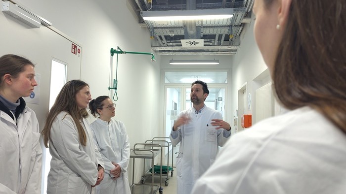 © IKE-B A man in a lab coat is standing in a laboratory hallway, speaking to four students who are also wearing lab coats.