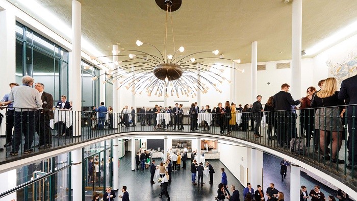 There are many people standing in a large foyer talking to each other.