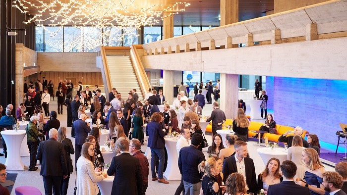 Numerous festively dressed people in a brightly decorated foyer at a standing reception.