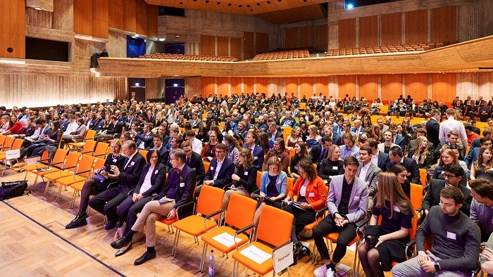 Numerous, festively dressed people are sitting in rows in a hall.