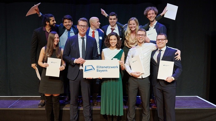 A small group of festively dressed young people stand laughing on the stage with their certificates.