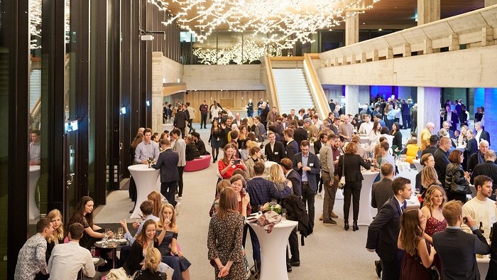 Numerous festively dressed people in a brightly decorated foyer at a standing reception.