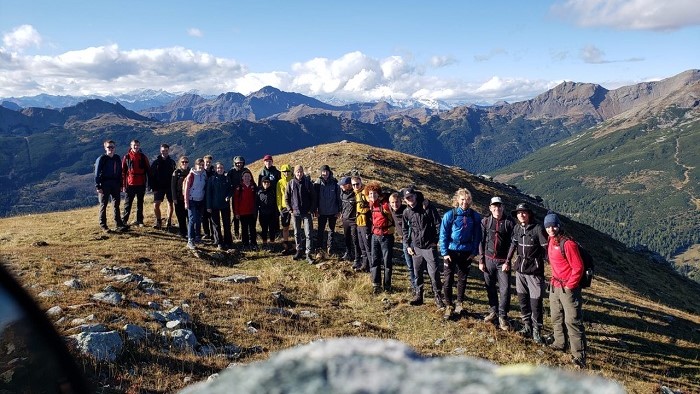 Some young people on a summit in front of a panorama view of mountains