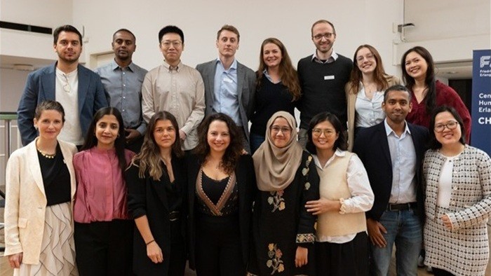 © FAU / Internationales Doktorandenkolleg „Business and Human Rights“ Eine Gruppe von Konferenzteilnehmenden steht in zwei Reihen vor einem Banner in einem hellen Raum und posiert für ein Gruppenfoto.