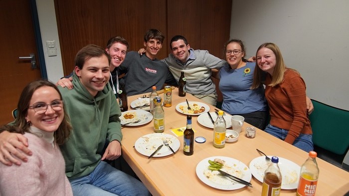 Students sit arm in arm around a table with finished plates.