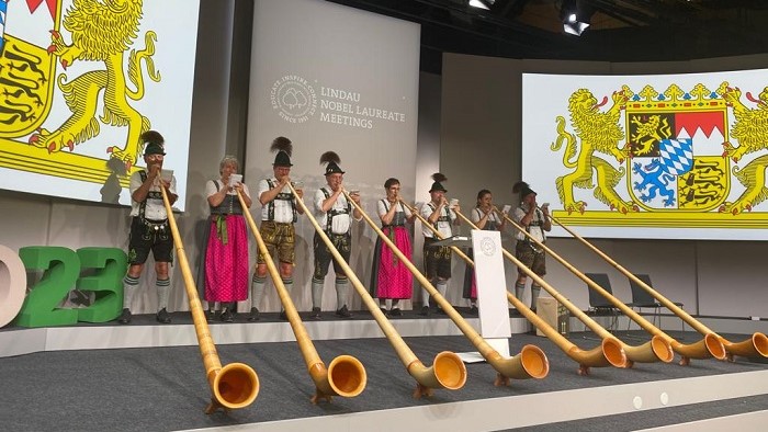 Alphorn players perform on a stage in front of the Bavarian coat of arms