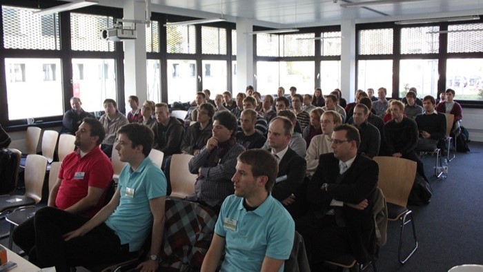 Das Bild zeigt eine Gruppe von Menschen, die in einem hellen Seminarraum aufmerksam einer Präsentation zuhören.