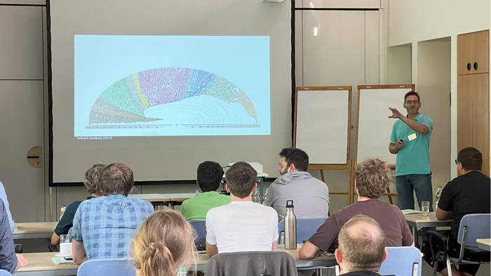 Ein junger Mann hält einen Vortrag vor Studierenden und Dozenten.
