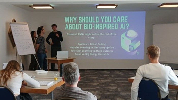 Mehrere junge Menschen halten eine Präsentation über bio-inspirierte Künstliche Intelligenz vor einem kleinen Publikum in einem Seminarraum.