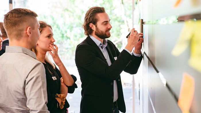 Three students stand in front of a wall with sticky notes.