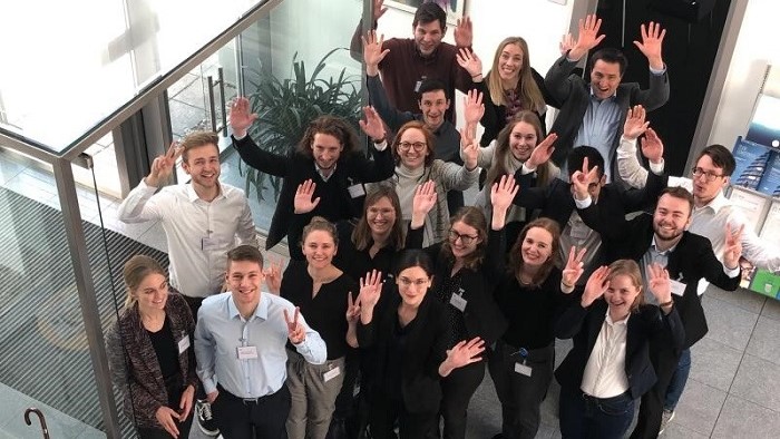 Gruppenbild junger winkender Menschen im Eingangsbereich eines Unternehmens.