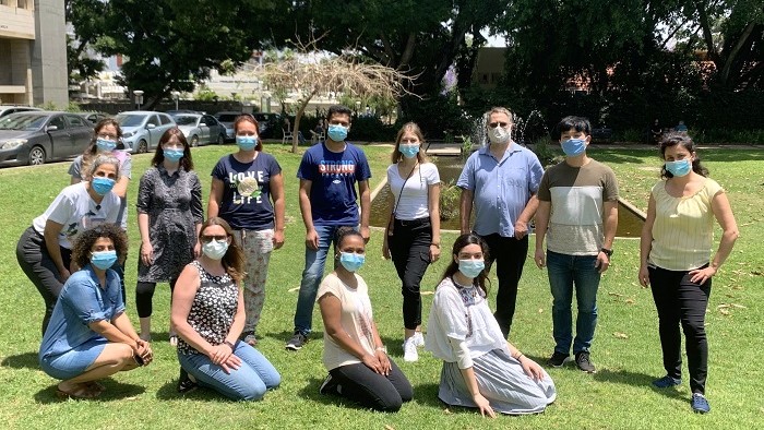 Group photo of Prof. Steffen Jung, his research team and Katharina Knab on a meadow on the campus of the Weizmann Institute.