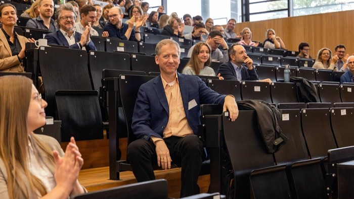 Das Bild zeigt einen Hörsaal mit mehreren Reihen, in denen Teilnehmende sitzen und einer Veranstaltung folgen.