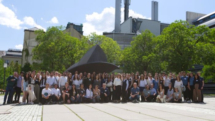 The picture shows a group of about 80 people gathering together for a group picture outside and smiling into the camera.