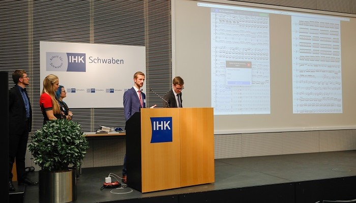 Five people at a speaker's desk with a projection in the background.