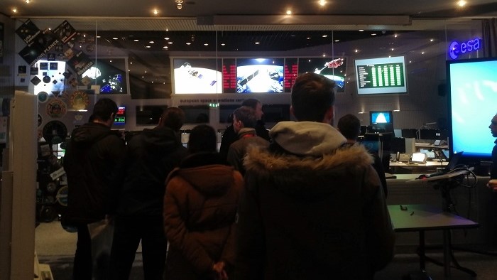 Young people stand in the room, which is equipped with many screens on the walls.