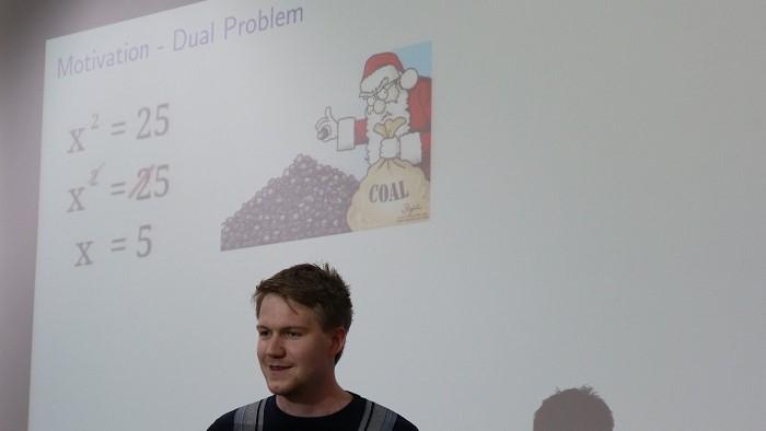 © Fabian Roll Der Vortragende Nathanael Schilling steht vor einer Projektionsfläche.