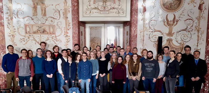 Eine Gruppe von Frauen und Männern steht vor der Eingangstür in einen herrschaftlichen Saal einer Residenz.