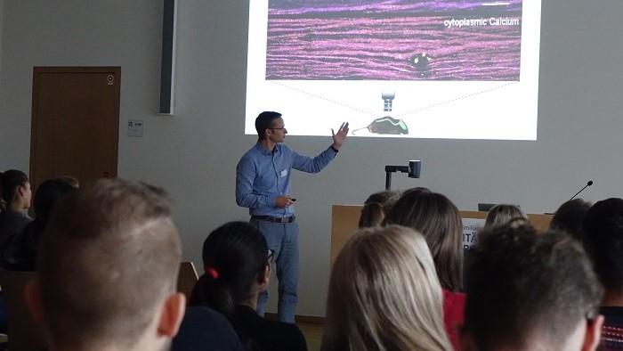 The speaker points to a projection surface with his hand.