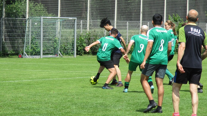 Junge Männer und Frauen beim Fußballspielen auf dem Spielfeld.