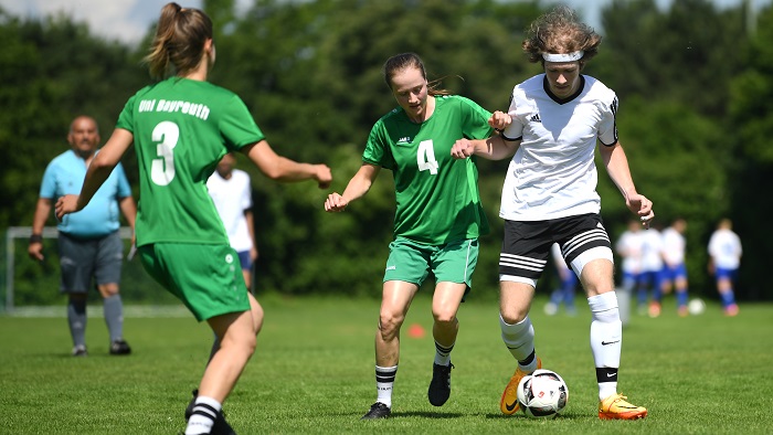 A young woman and a young man in soccer jerseys fight for the ball on the field.