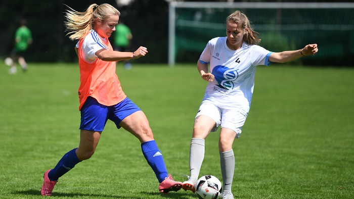 wei junge Frauen in Fußballtrikots kämpfen auf dem Spielfeld um den Ball.