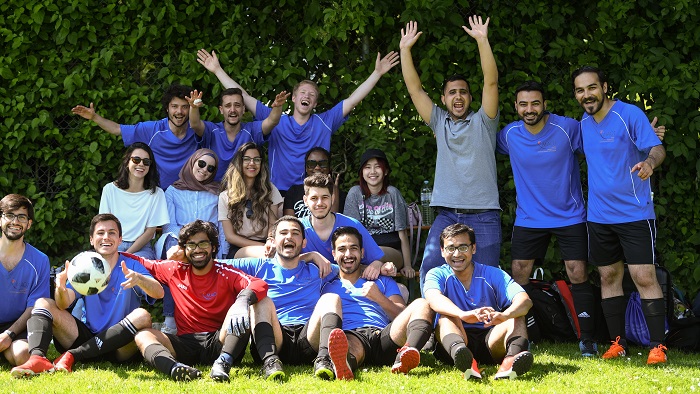 Eine Gruppe junger Männer in Fußballtrikots posiert zusammen mit weiteren jungen Frauen und Männern für ein Gruppenbild.