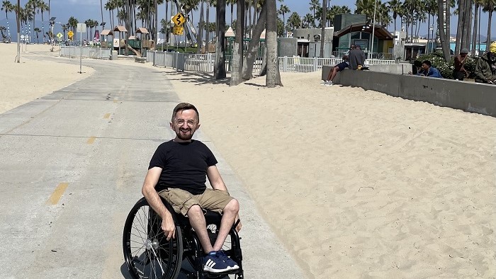 A young man in a wheelchair on a sandy beach with palm trees