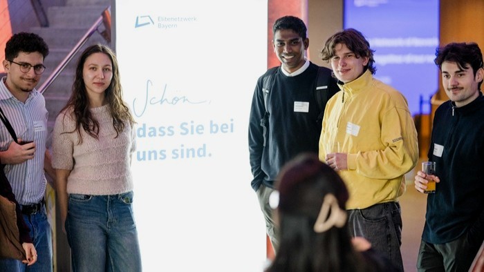 Gruppe von Teilnehmenden steht neben einem Banner des Elitenetzwerks zusammen für ein Gruppenfoto.