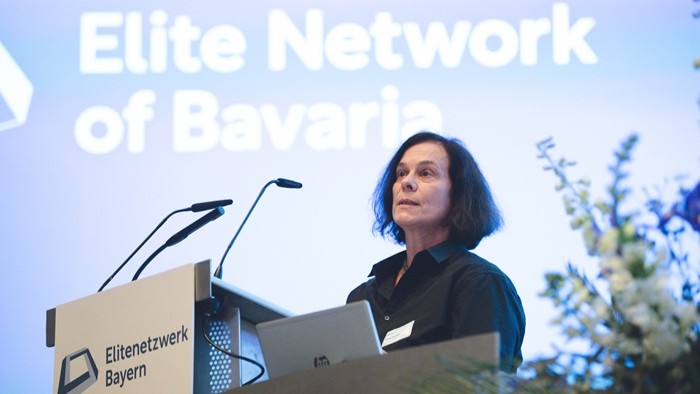 Eine Rednerin steht an einem Pult vor einer großen Präsentationsfläche.