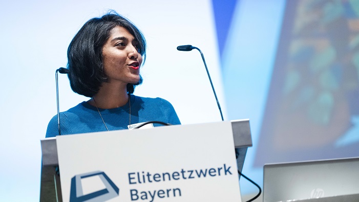 A young woman is standing behind a lectern and is speaking to the audience.