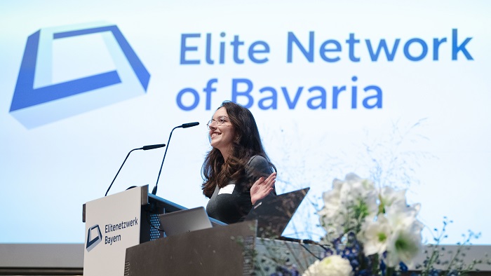 A young woman is standing behind a lectern and is speaking to the audience.
