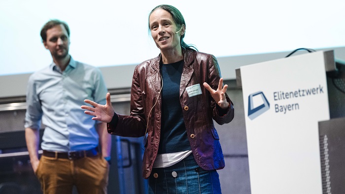 A woman and a man are standing on stage and speaking to the audience.