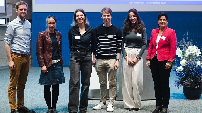 A group of six people are standing on stage and are smiling into the camera for a group picture.